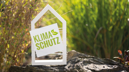Weißes Haus mit der Aufschrift Klimaschutz umgeben von Pflanzen