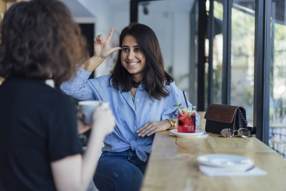 Zwei Damen unterhalten sich in Gebärdensprache beim Kaffeetrinken Zwei Damen unterhalten sich in Gebärdensprache beim Kaffeetrinken
