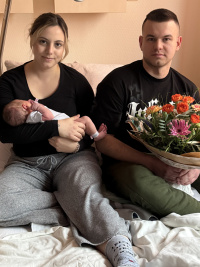 Neujahrsbaby 2026 mit Mama Felicitas und Papa Alexej lternporträt im Krankenhauszimmer: Felicitas Benoit hält Neujahrsbaby Malia im Arm, Vater Alexej Bernowsky sitzt daneben mit einem Blumenstrauß.